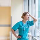 exhausted female nurse leaning on a window in a hospital corridor