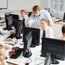 A group of teenage students focused on their studies in an Information Technology classroom, with the professor explaining the task.