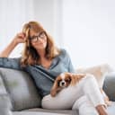 Shot of happy middle aged woman relaxing on the sofa at home with her cavalier puppy
