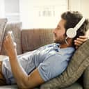 Man wearing headphones lying on a couch listening to music on smartphone