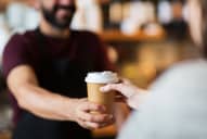 Barista hands single-use coffee cup to customer