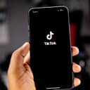 A person holding a phone with a TikTok logo on the screen