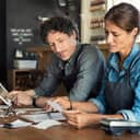 couple of managers wearing aprons examining financial documents and bills in their coffee shop