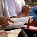 Group of Christian friends gathered and praying over the Bible together.