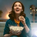 Young woman watching projector, TV, movies with popcorn in the evening. Girl spending time at home.