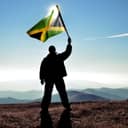 man waving a Jamaican flag on top of a hill