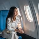 Asian woman sitting in a seat in an airplane and looking out the window going on a trip.