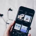 A person holds an iPhone 6 with the Spotify app open on the 'Home' page.