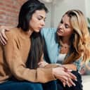 young woman comforting her distressed female friend on the sofa at home