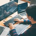 A young developer writing code on multiple computers simultaneously