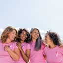 Four women in a row wearing pink t-shirts hugging and holding each other