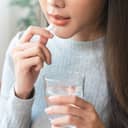 close-up of a young woman taking a pill and holding a glass of water
