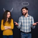 Man and woman standing next to each other in front of a black wall with horns drawn on the wall above the woman's head and circle above the man's head