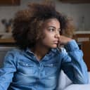 pensive teenage girl sitting on a couch at home with hand on her cheek, looking away