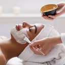 Close-up of a beautician applying a clay mask to the face of a young woman.