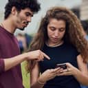 Young woman typing on her phone while her male friend is telling her the steps she should follow.