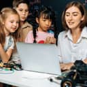 young female teacher coding to show children how to program robots in a STEM class