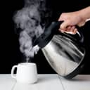 Person pouring boiling water from a kettle into a cup