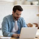 young man working remotely on a white laptop in his modern kitchen