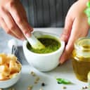 Woman hands making italian pesto in bowl. Ingredients - basil, lemon, parmesan, pine nuts, garlic, olive oil and salt on rustic wooden background. Top view, flat lay, copyspace