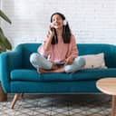 A young woman sitting on a couch with headphones on her head listening to music