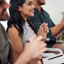 Close-up of three business professionals at a seminar, clapping and smiling after a presentation in the office.