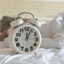Person lying in bed with alarm clock in the foreground