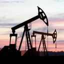 two oil drilling derricks in a desert field with a beautiful, colorful sky in the background