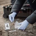close-up of a crime scene investigator collecting a pistol bullet from the ground