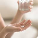 A closeup of a person holding a pill in one hand and a glass of water in another