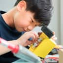 Asian boy engaged in building a robotics project using wires and computer components