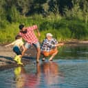 Boy joyfully skimming stones on a lake with his dad and granddad.