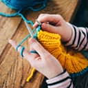 A woman knitting a yellow and blue sweater
