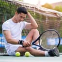 tired and disappointed male tennis player sitting on the court next to the net