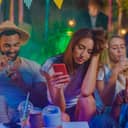 Disappointed girl looking at her smartphone as she sits among people at a party
