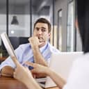 Man skeptically listening to a woman present notes to him in an office