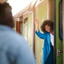 A smiling woman waving to her friend as she's getting on a train