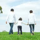 A little girl holding her parents' hands while walking in a park