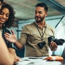 A male photographer holding a camera talking with his clients