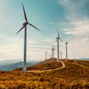 Wind turbines on a sunny mountain landscape with a curvy road running through an eolic park