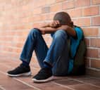 Sad schoolboy sitting on the floor leaning against the wall