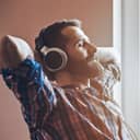 Man with calm expression on his face sitting on a chair wearing headphones with arms behind the head