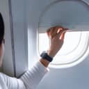 Close-up of a female passenger lifting the airplane window shade before landing.