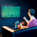 Man playing soccer video game on a sofa holding a gaming console controller and cheering