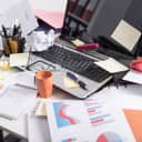 Cluttered work desk with papers, laptop, coffee mug and sticky notes