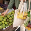 A woman choosing fruit at a farmers market and placing them in reusable bags