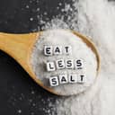 "Eat less salt" spelled out in plastic letter cubes placed on a wooden spoon full of granulated salt.