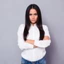 A woman with an angry look on her face standing with her hands crossed