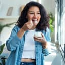 portrait of a young, happy woman eating yogurt in her living room at home