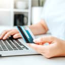A young woman browsing the internet and holding a credit card in her hand.